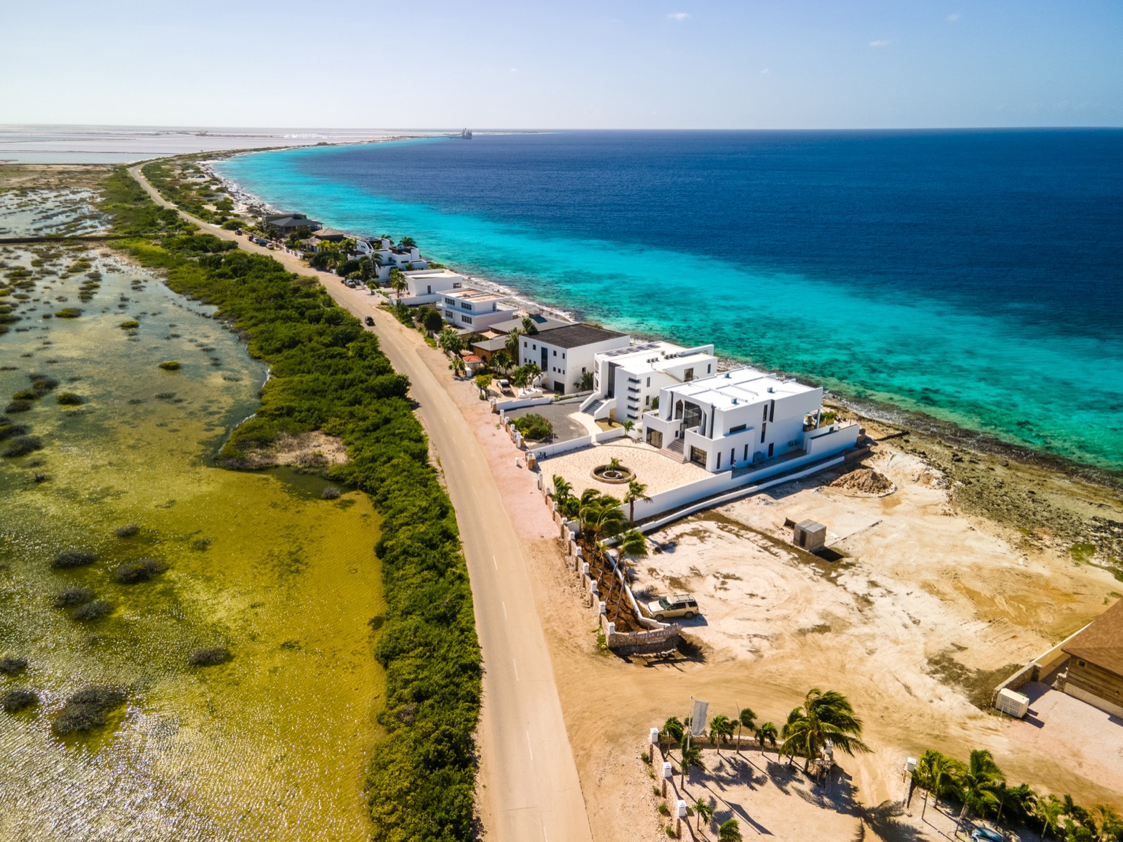 Aerial view of a luxury modern white villa on the Bonaire coast, situated between the turquoise Caribbean Sea and natural green mangroves.